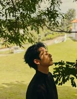 王鹤棣于静谧园林中小憩，黑色长衫衣袂轻垂，面容沉静如水，与周遭环境浑然一体