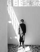 王鹤棣坐在石阶上，姿态放松却难掩风采，黑色长衫的下摆铺展开，与环境中的石材肌理相映成趣