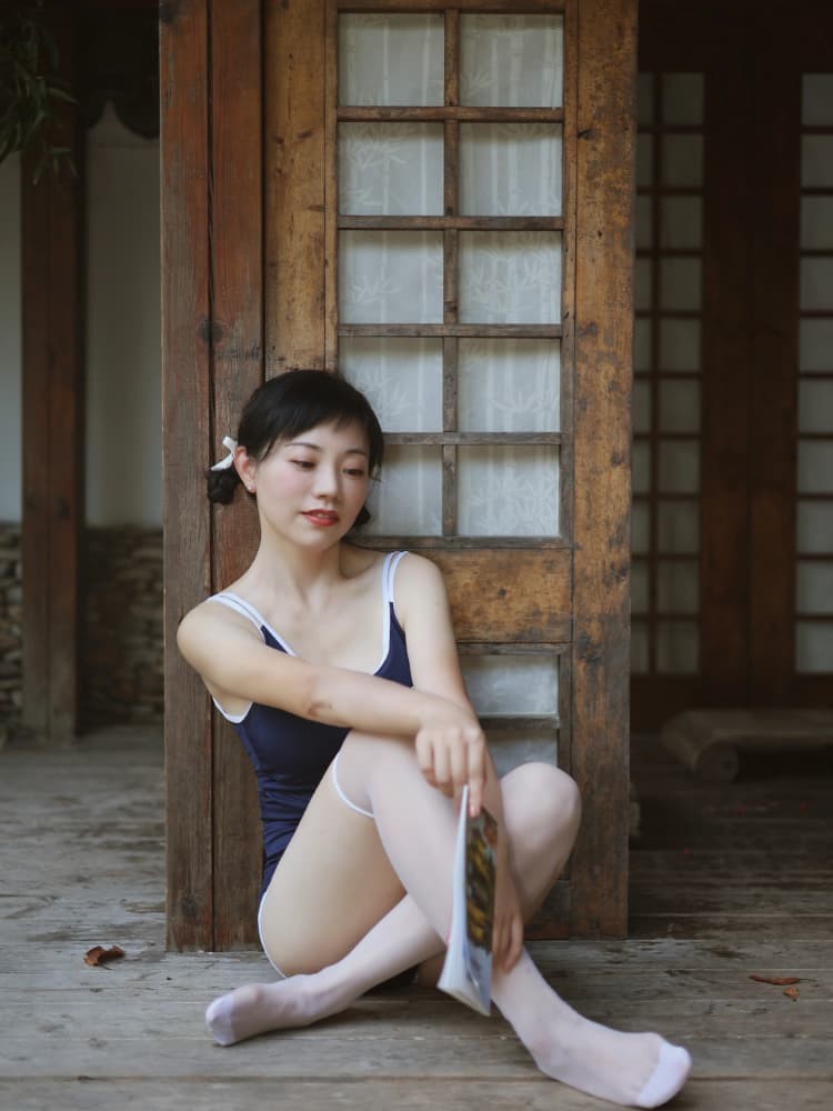 女孩身着藏青色死库水，依靠在墙壁旁，午后阳光在她身上投下斑驳光影，眼神清澈望向远方