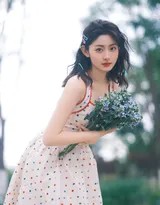 特写镜头下，赵晴手拈一朵白色小野花，与裙上的波点相映成趣，她低头垂眸，长睫在脸颊投下阴影，嘴角含着一抹若有若无的笑意，温柔至极。