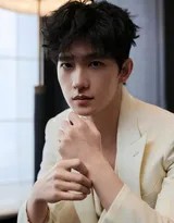 杨洋坐在木椅上展露淡然微笑，白色西装与静谧环境融合，尽显惬意午后时光