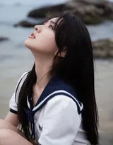 梁洁弯腰伸手触碰涌上沙滩的海浪，表情专注而好奇，阳光在水面和她身上洒下跳跃的金色光斑