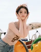 她倚靠在岸边的礁石上，手臂舒展，望向远方的海平面，神情静谧而充满故事感