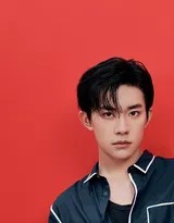 易烊千玺侧身立于红色幕布前，深邃目光凝视远方，蓝色衬衫的丝质光泽在光影中流淌