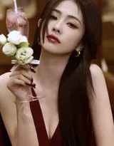 她微微仰头浅笑，红裙肩带滑落一丝香肩，手中果汁杯沿留下淡淡唇印，慵懒中透着不经心的妩媚