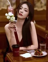 逆光中白鹿的轮廓泛起朦胧光晕，红裙褶皱如绽放玫瑰，她低头凝视杯中气泡升腾的模样专注而温柔