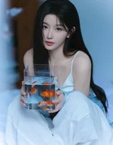 孔雪儿身着蓝色细肩带背心，微卷长发披肩，在柔和光线下托腮凝望，眼神清澈而宁静。