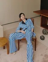 秦岚倚靠墙边，双手插兜，蓝白条纹西装套装在柔和光线下呈现细腻质感，她直视镜头，表情从容淡定，尽显独立女性风范