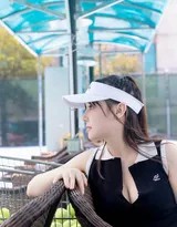 中场休息时倚靠球网，微红脸颊挂着汗珠，阳光在棒球帽檐下投出俏皮阴影