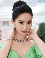 刘亦菲身着一袭翡翠流光深V长裙侧身立于罗马古典石廊前，微卷长发轻披肩头，眼眸低垂间流转着温柔而神秘的光泽，身后斑驳的古墙与她的现代优雅形成时空对话
