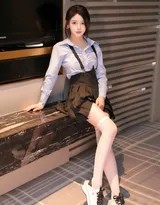 爱酱倚靠在桌边，蓝色衬衫袖口卷起，她手持道具，嘴角微扬展露标志性笑容，俏皮中带着甜蜜