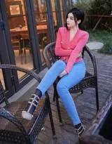 龙雪儿低头浅笑，红色上衣领口微敞，牛仔裤膝盖处撕裂设计展现街头风，高跟鞋细跟支撑优雅体态