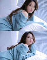 女孩身着蓝衣倚靠窗边，百叶窗的光影如琴弦般掠过她的身体，她微微侧首，长发轻垂，在柔和的光晕中展露一抹沉思般的静谧微笑。