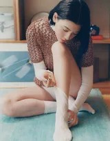 她慵懒地蜷在复古沙发上，指尖轻触嘴唇陷入沉思，暖色调光线让整个场景充满故事感