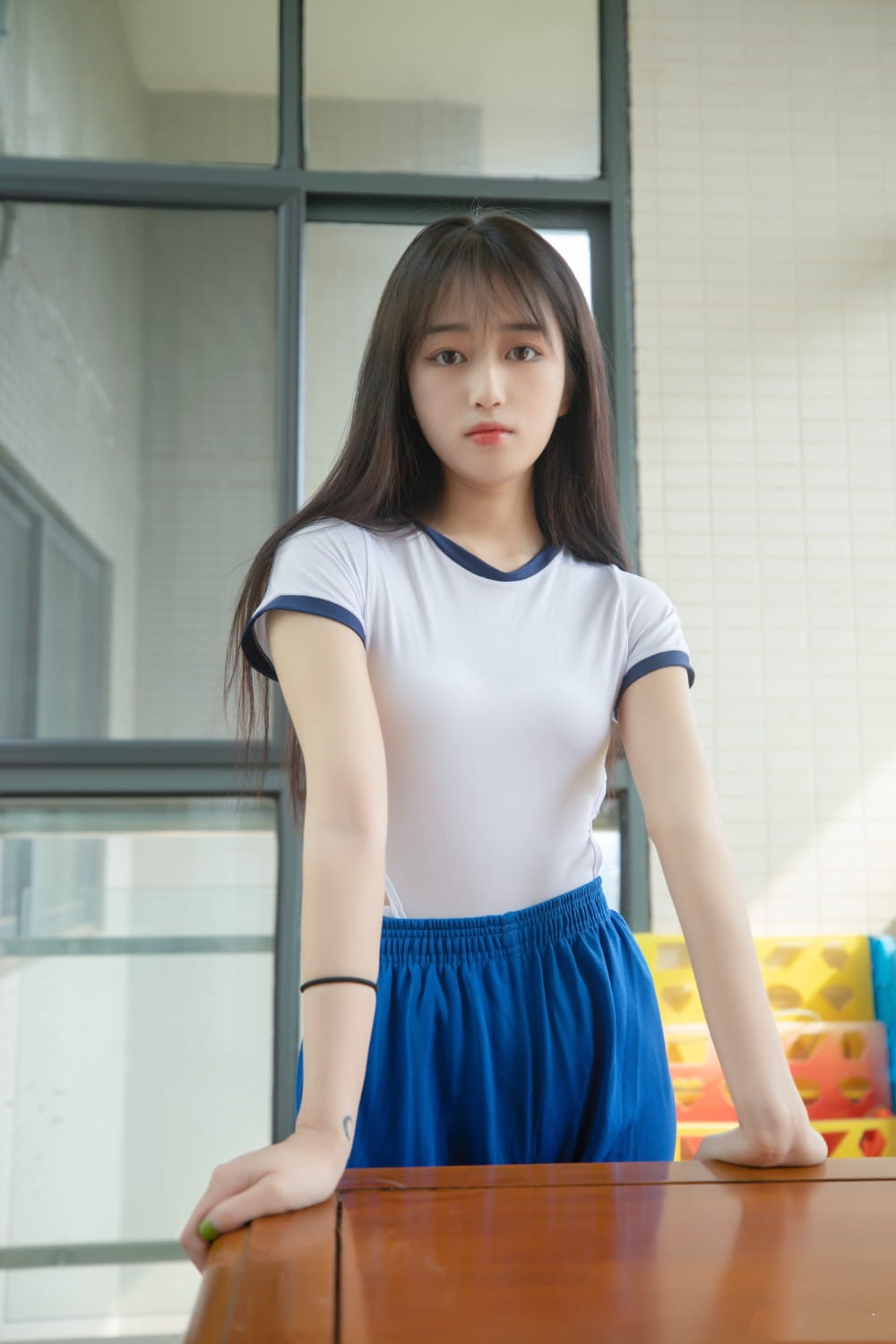 女生在教室走廊灿烂微笑，背后是绿意盎然的校园，整个画面充满校园青春气息