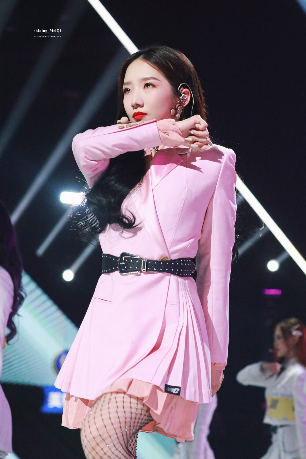 孟美岐侧身舞动，丝袜闪耀光泽，腿部伸展如优雅天鹅，舞台背景光影交错