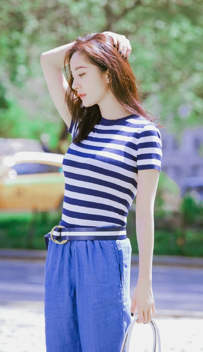 杨幂俏皮地半躲在一块蓝色背景板后，眼神狡黠笑容甜美，充满童趣