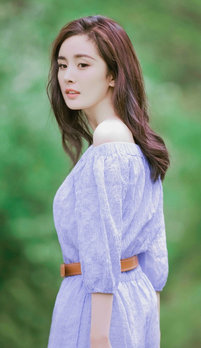 杨幂身穿粉色系上衣，坐在地上手持画具，身边环绕着彩色玩具，笑容天真浪漫