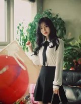 美女微笑凝视镜头，白衫黑裙衬托出知性魅力，背景柔和温馨