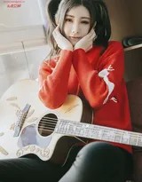 莫小琪怀抱吉他倚靠墙边，双马尾与暖色毛衣在柔和光晕中显得格外温柔