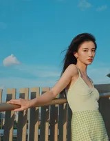 女孩倚靠天台围栏展露微笑，格子裙在阳光下色彩鲜明，长发随风扬起一抹温柔