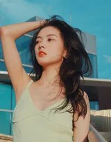 轻倚白墙午后光影斑驳，格子裙褶轻铺地面，少女低眉浅思时光安然