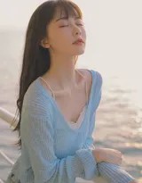 蓝衣少女侧身倚靠白色游轮栏杆，海风拂起她的长发，身后是浩瀚无垠的蔚蓝海面