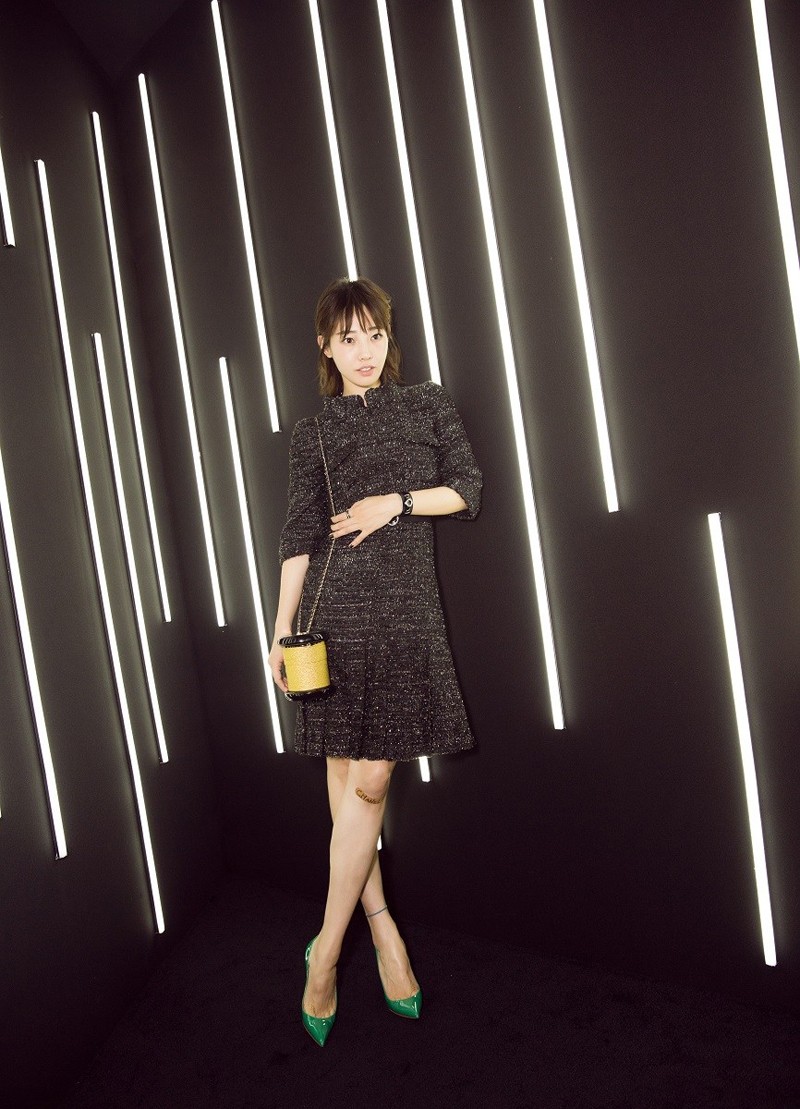 白百何单手轻抚手臂，黑色刺绣裙的精致细节在灯光下闪耀，整体姿态娴静优美