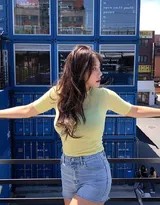 女孩倚靠在集装箱上，双臂舒展，姿态放松，午后的阳光为其轮廓镀上一层金边