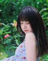 女孩蹲在草丛中，指尖轻抚沾满露珠的草叶，专注的神情中带着发现自然的惊喜与温柔。