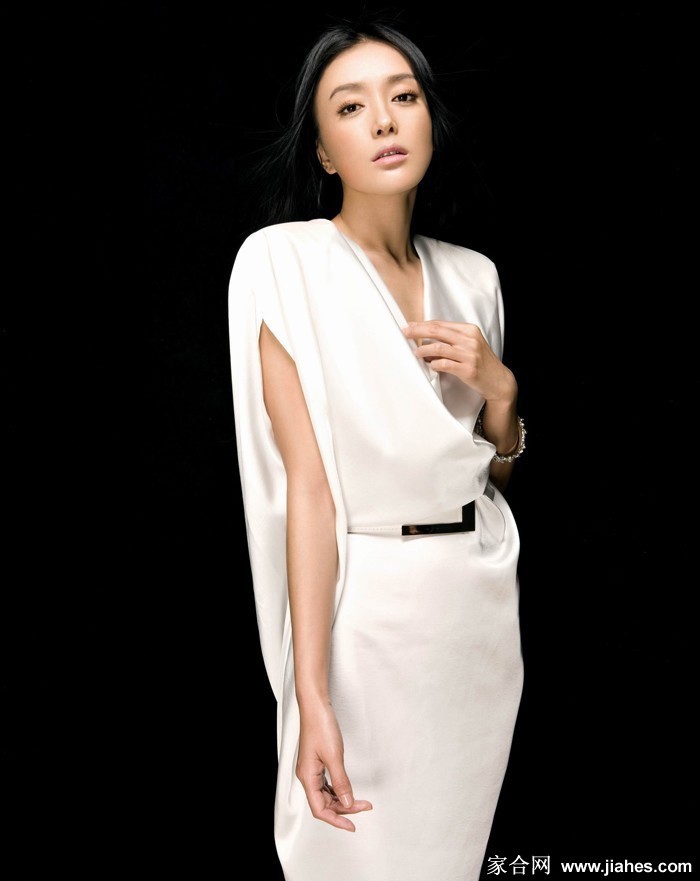 秦岚一袭酒红长裙置身沙滩，赤足坐于树桩尽显自然风情，海风拂面故事感十足