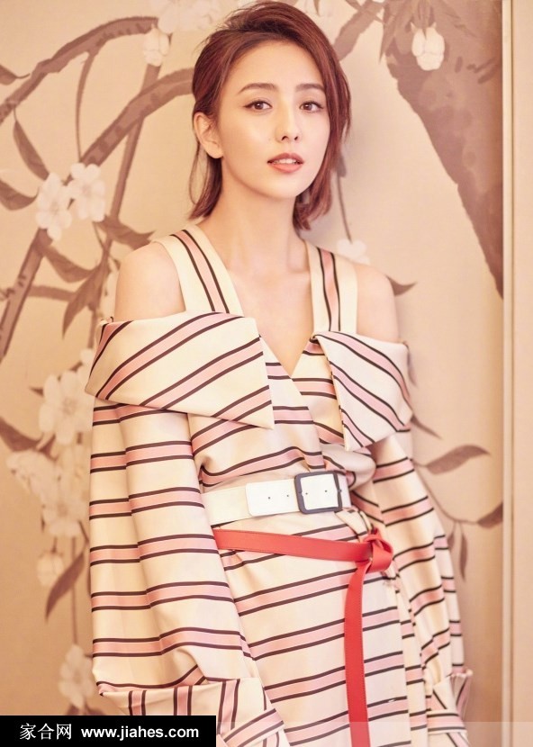 佟丽娅倚靠窗边，条纹衬衫袖口轻挽，笑容明媚散发出自然知性美