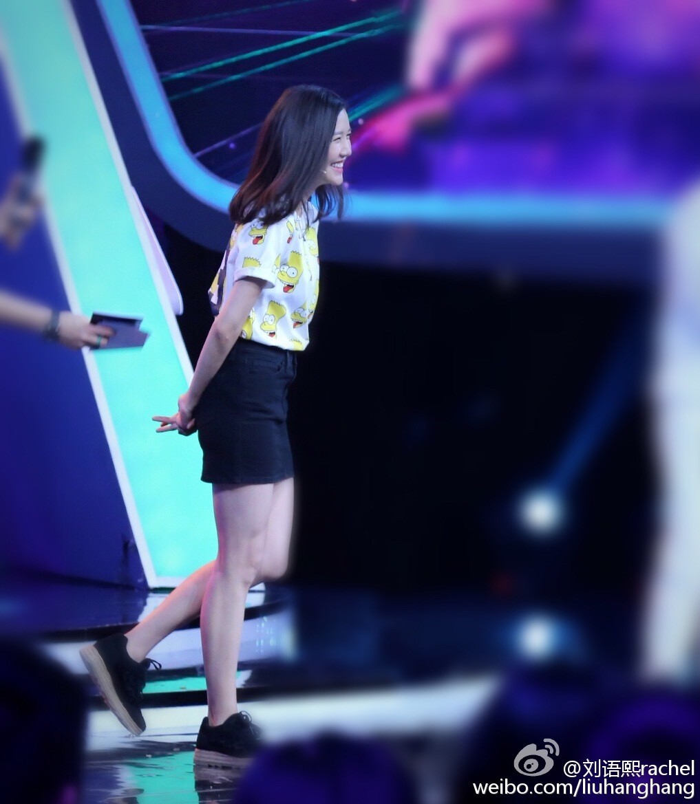 刘语熙侧身聆听，丝袜勾勒出优雅腿部线条，聚光灯下裙摆微扬