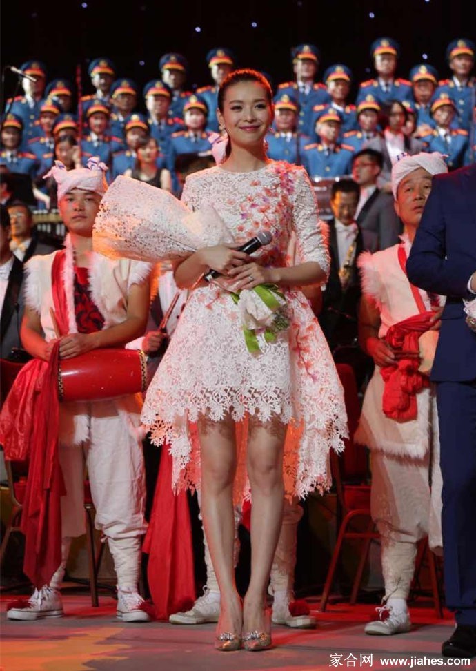 舞台中央，栗坤身着简约裙装，手持话筒专注主持，聚光灯下身影修长而优雅