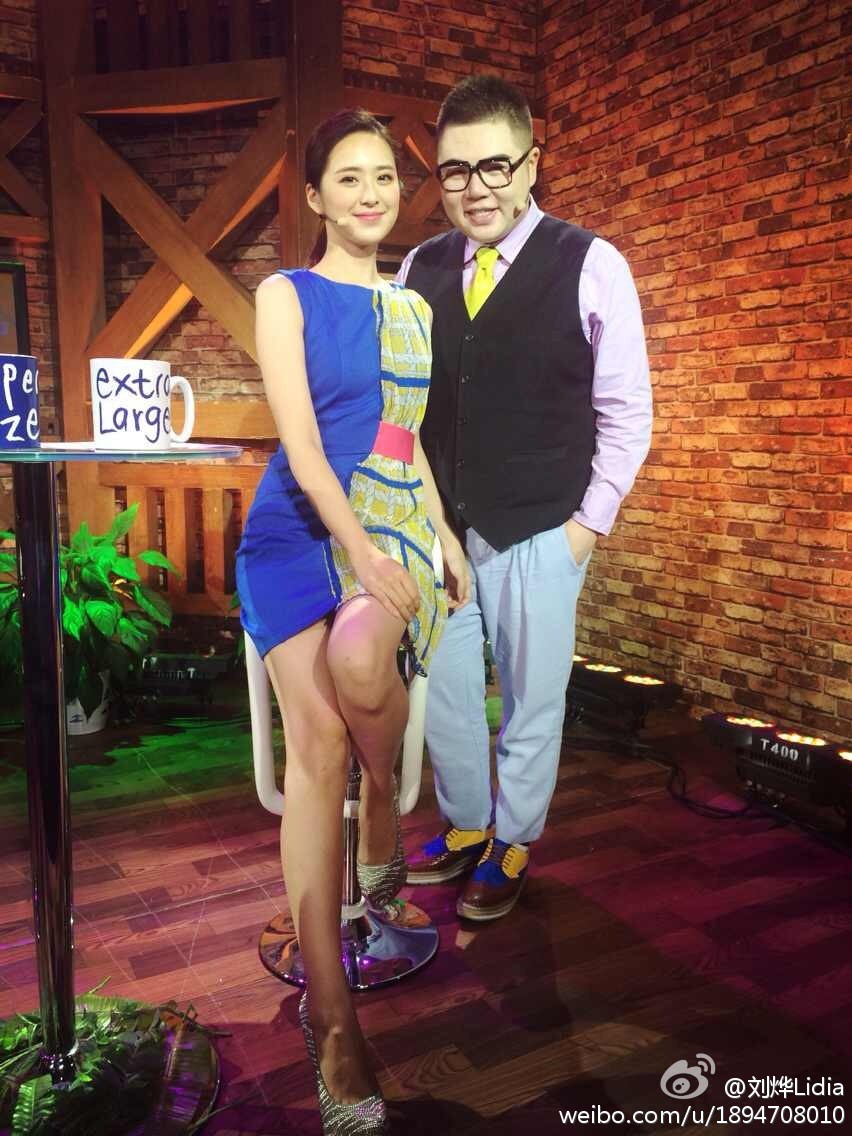 聚光灯下刘烨手持话筒专注主持，高跟鞋与丝袜勾勒出专业干练的腿部线条