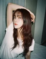 赵樱子身着简约白T恤侧坐床边，自然光勾勒出柔和侧颜与慵懒长发