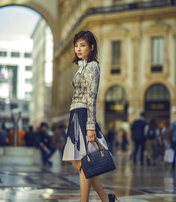 刘涛身着米白大衣倚靠石柱，冬日暖阳轻抚面庞展露温柔浅笑