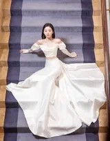 包上恩坐于楼梯底层，双手轻拢裙摆，阳光透过栏杆洒落，她神态安详如画中仙