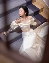 包上恩倚靠楼梯墙壁，抹胸设计凸显肩颈之美，她闭目沉思，氛围宁静而神秘