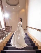 包上恩站立于楼梯光影交界处，白色长裙与暗色背景对比鲜明，她眼神坚定而柔美