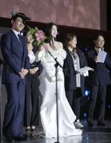 包上恩俯身整理裙摆，楼梯背景延伸纵深，她姿态优雅，仿佛时间在此刻静止