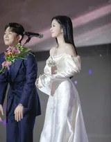 包上恩立于楼梯顶端，白色抹胸长裙映衬出神圣光晕，她张开双臂，宛若自由飞翔的精灵