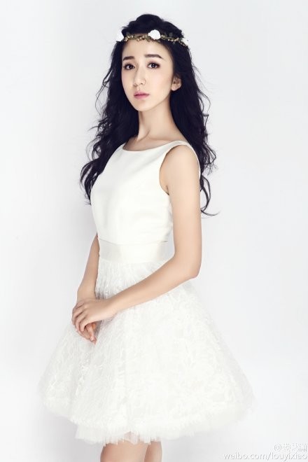 娄艺潇轻倚背景，白裙铺展如云，她低头浅笑尽显温柔娴静之美