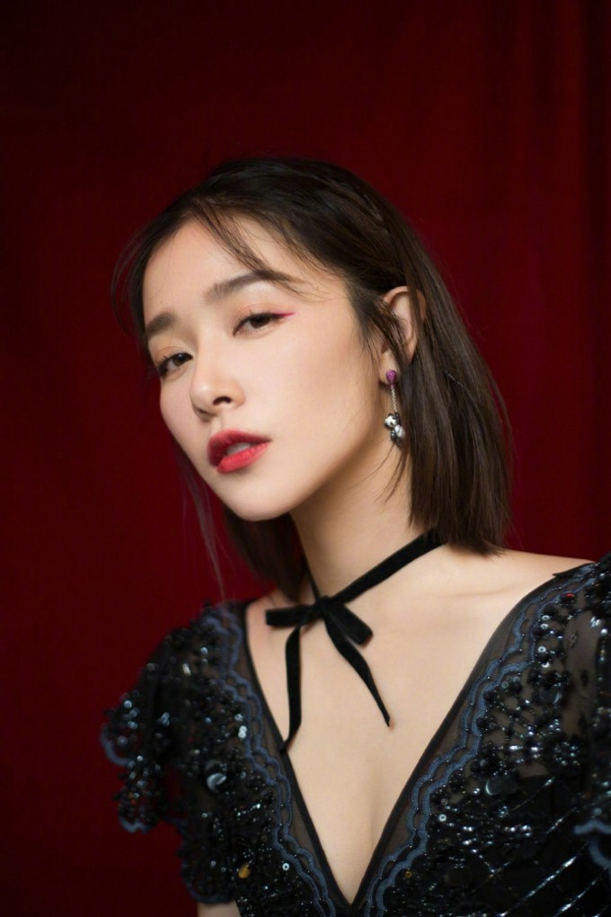 阚清子微抬下颌，灯光洒在肌肤上，黑色裙装与红唇形成经典魅惑对比