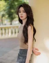 陈瑶身穿浅驼色针织背心漫步街头，回眸瞬间发丝轻扬眼神温柔，背景暖阳与木质墙面交织出浓郁秋日氛围