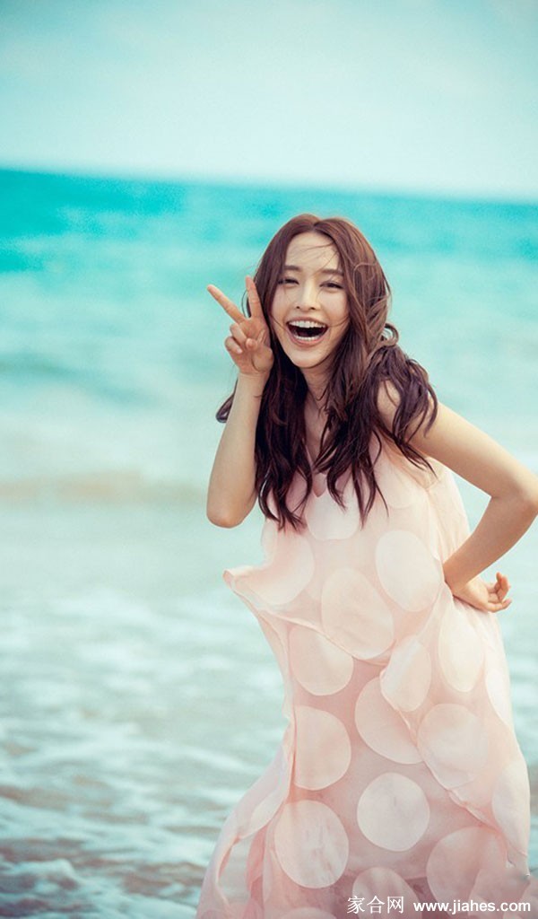 张俪身着牛仔泳衣侧身回眸，海风轻拂发丝，笑容自信而灿烂