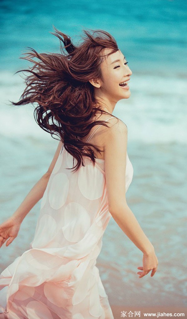 张俪倚靠海边围栏，手持冲浪板眺望远方，侧影轮廓在阳光下格外清晰