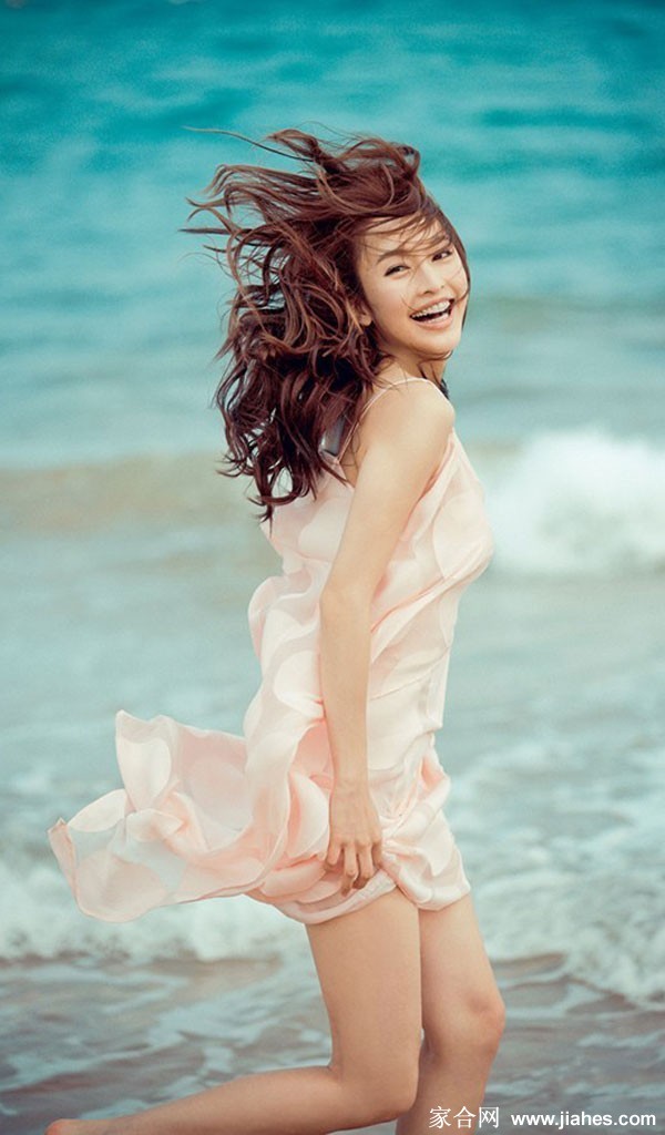 张俪坐在沙滩上，笑容温暖治愈，洋溢着无忧无虑的快乐与纯真