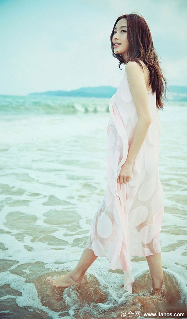 张俪赤脚漫步于沙滩，手提凉鞋，身后留下一串足迹，尽显悠闲惬意