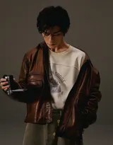 易烊千玺微笑面对镜头，皮衣与工装牛仔裤搭配随身听，尽显轻松自如的复古摩登型格，背景虚化突出人物